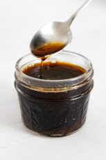 Photo of a glass jar and a spoonful of vegan Worcestershire sauce