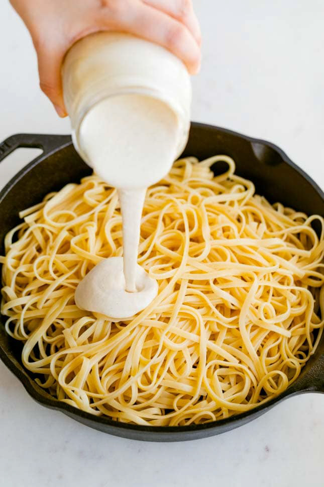 Photo of some vegan Alfredo sauce being poured onto noodles