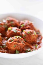 Side picture of a shallow white dish with vegan meatballs garnished with some chopped parsley