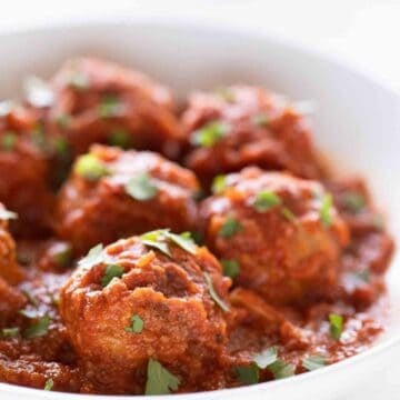 Side picture of a shallow white dish with vegan meatballs garnished with some chopped parsley