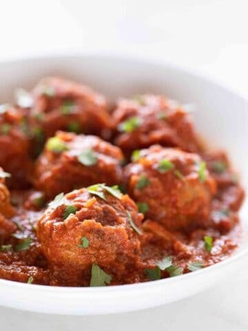 Side picture of a shallow white dish with vegan meatballs garnished with some chopped parsley