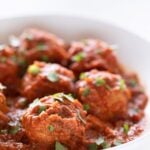 Side picture of a shallow white dish with vegan meatballs garnished with some chopped parsley with a heading