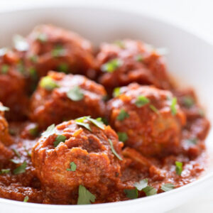 Square picture of a shallow white dish with vegan meatballs garnished with some chopped parsley