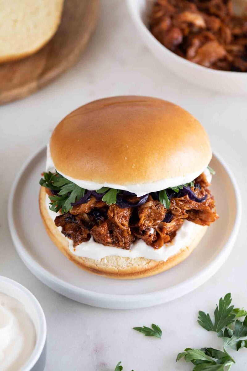 Photo of a dish with a vegan jackfruit pulled pork sandwich onto a white blackground
