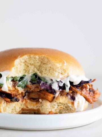 Side photo of the inside of a jackfruit pulled pork sandiwch onto plate with vegan mayo, cooked red cabbage and some parsley