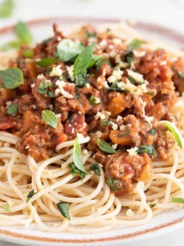 Close-up photo of a dish with spaghetti and vegan bolognese with some vegan Parmesan cheese and fresh basil on top