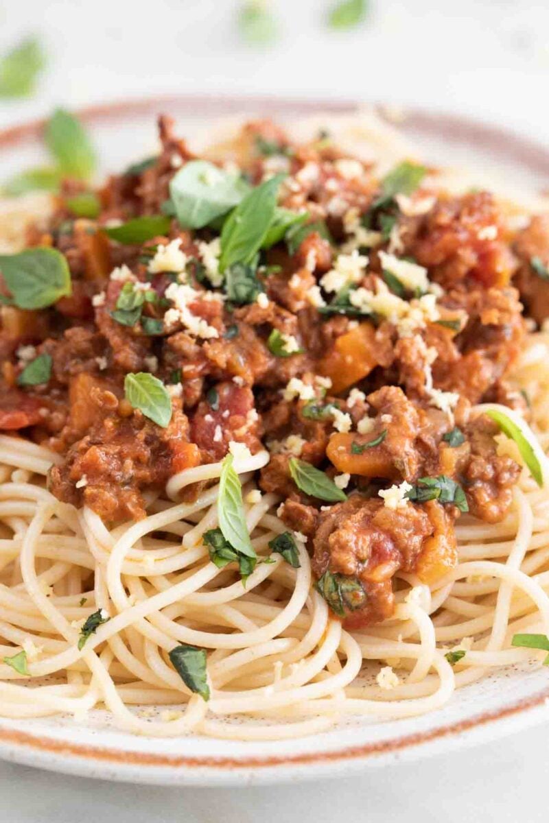 Close-up photo of a dish with spaghetti and vegan bolognese with some vegan Parmesan cheese and fresh basil on top