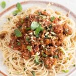 Close-up photo of a dish with spaghetti and vegan bolognese with some vegan Parmesan cheese and fresh basil on top with a heading