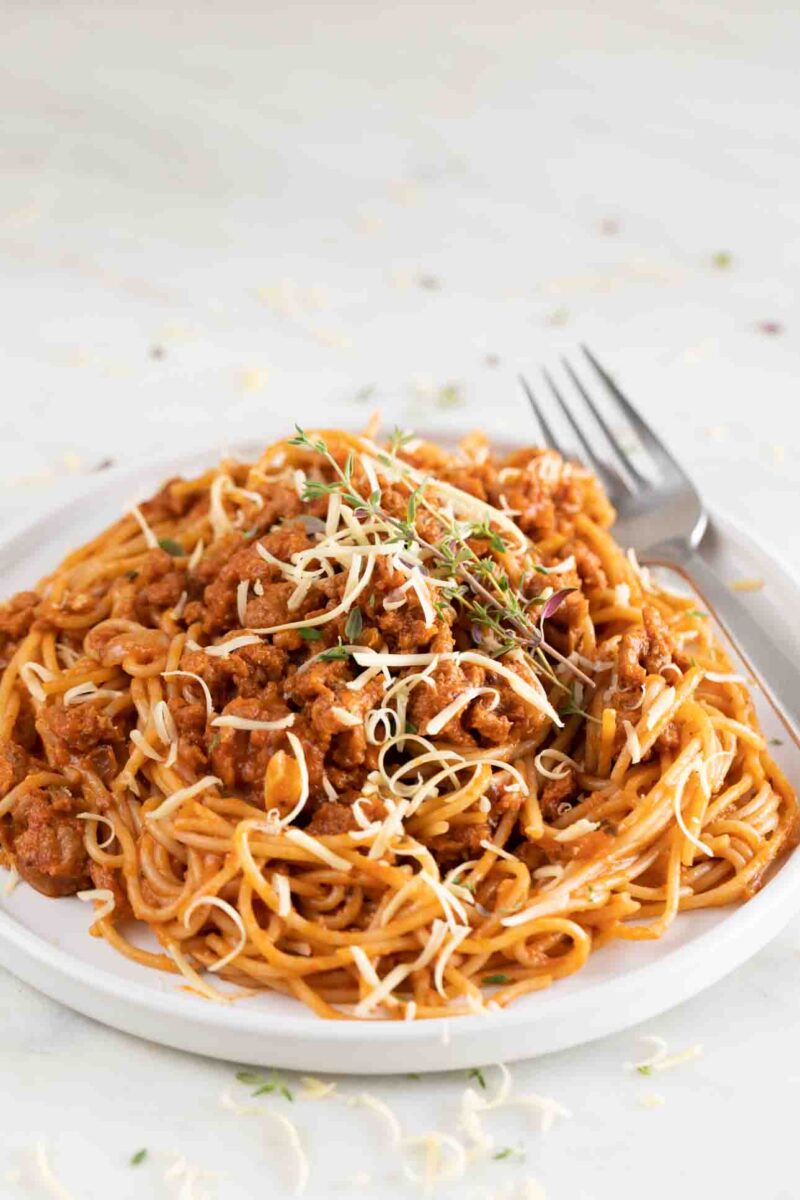 Photo of a dish with vegan spaghetti topped with vegan cheese and fresh herbs, and a spoon