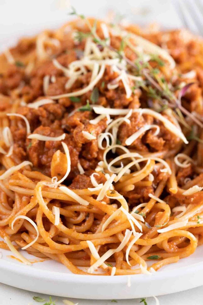 Close-up photo of a dish of vega spaghetti with some fresh herbs and vegan cheese on top