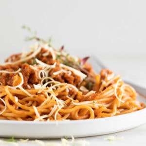 Square picture of a dish with vegan spaghetti garnised with some vegan cheese