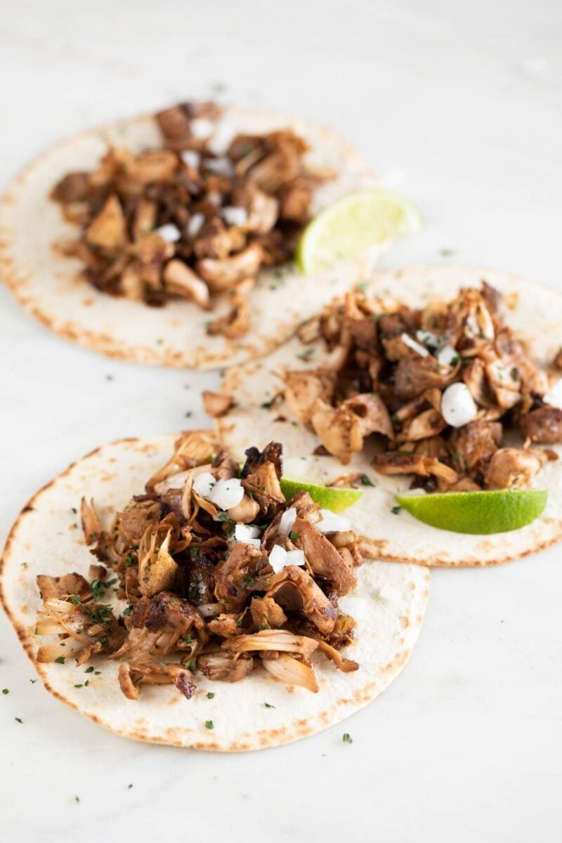 Photo of 3 jackfruit carnitas served with tortillas, lime wedges, diced onion and chopped cilantro