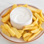 Square photo of a dish with French fries and a small bowl with vegan aioli.