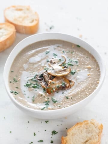 Photo of a bowl of vegan mushroom soup, topped with some sautéed mushrooms, chopped parsley, and a drizzle of coconut milk.