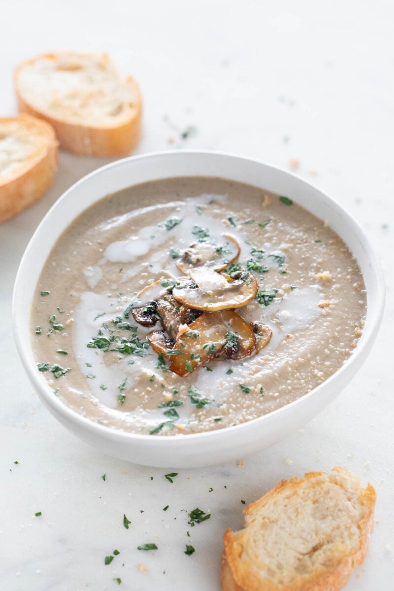 Photo of a bowl of vegan mushroom soup, topped with some sautéed mushrooms, chopped parsley, and a drizzle of coconut milk.