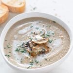Photo of a bowl of vegan mushroom soup, topped with some sautéed mushrooms, chopped parsley, and a drizzle of coconut milk with a heading.