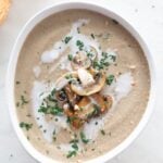 Overview photo of a bowl of vegan mushroom soup with some bread slices, chopped parsely, a drizzle of coconut milk and some sautéed mushrooms with a heading.