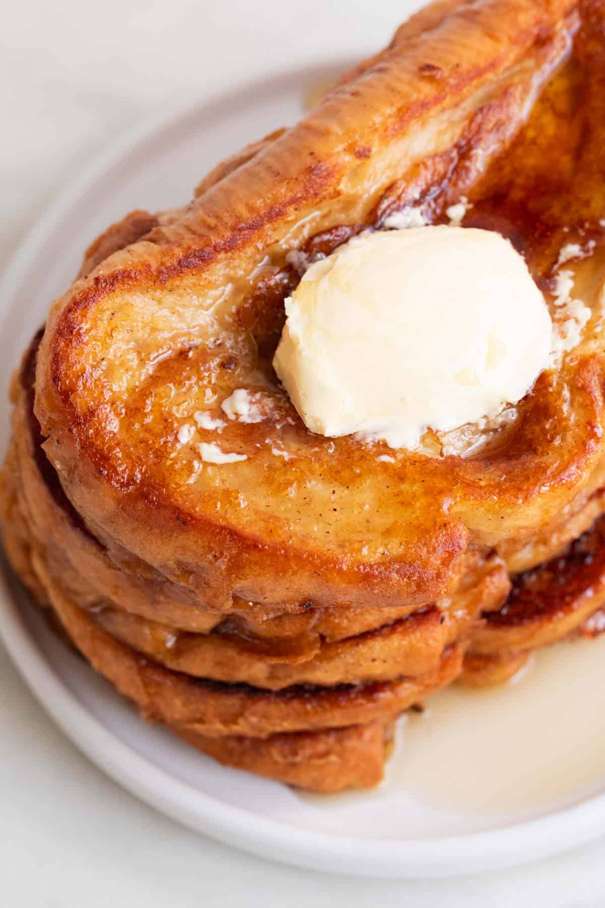 Overview of a stalk of vegan French toast on a plate with some maple syrup and vegan butter on top.