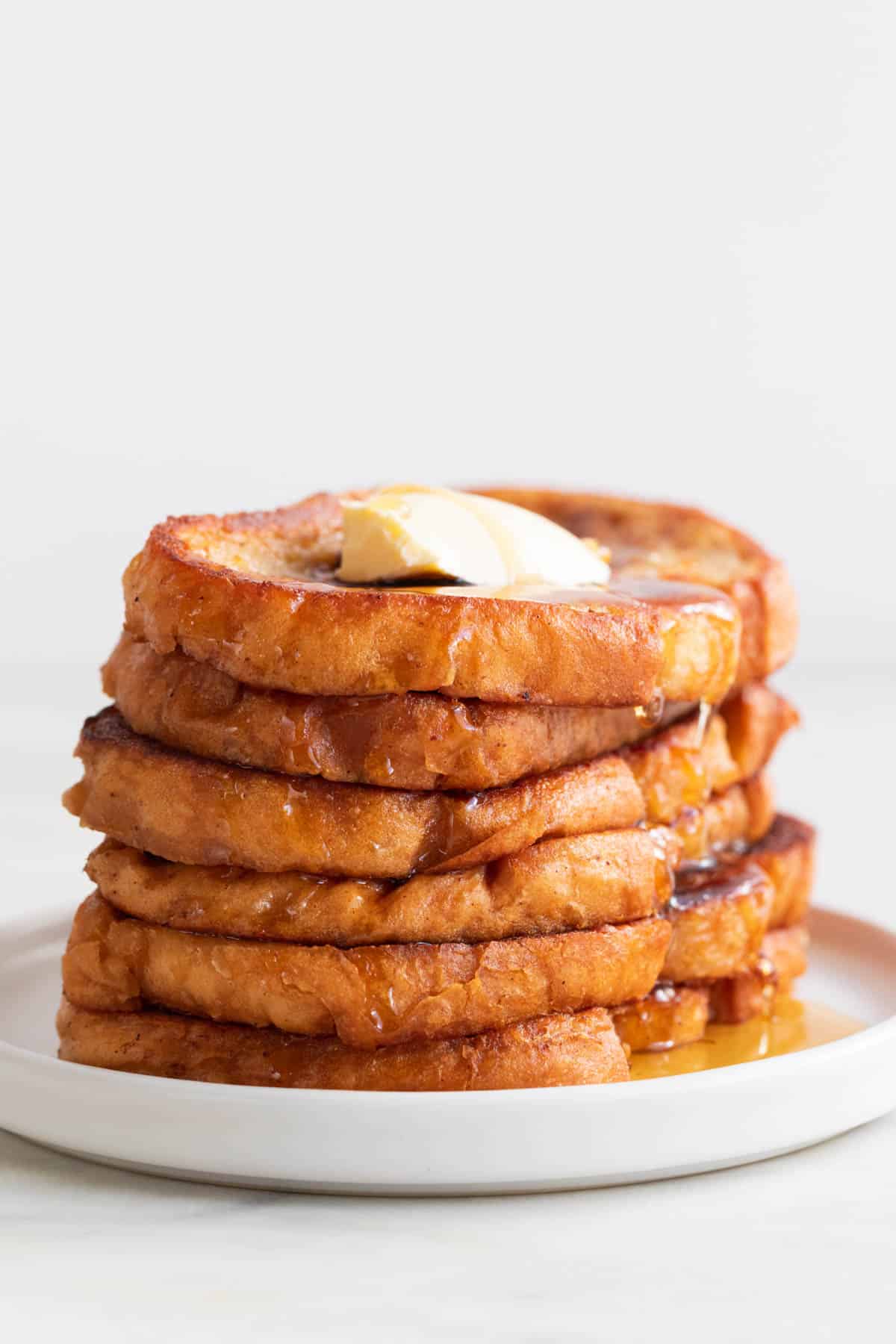 Stalk of vegan French toast on a plate with some maple syrup and vegan butter on top.