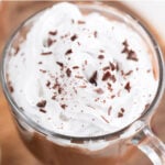 Close up of a jar of vegan hot chocolate topped with vegan whipped cream and chopped dark chocolate.