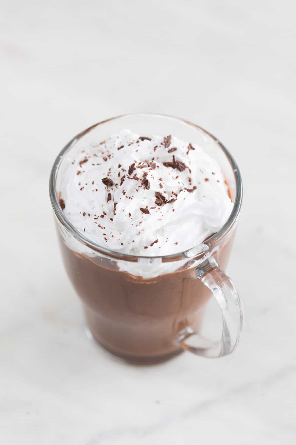 A jar of vegan hot chocolate with vegan whipped cream and chopped dark chocolate on top.