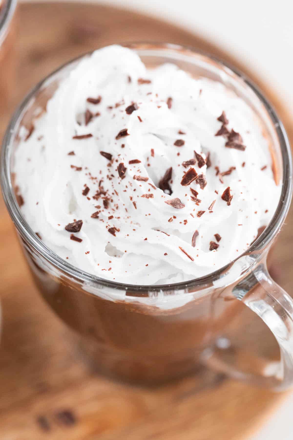 Close up of a jar of vegan hot chocolate topped with vegan whipped cream and chopped dark chocolate.