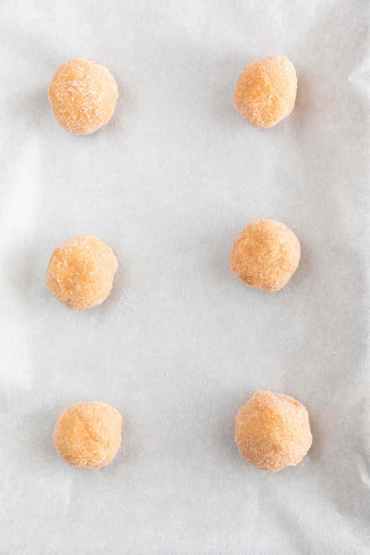 Cookie balls rolled in sugar onto a lined baking sheet.