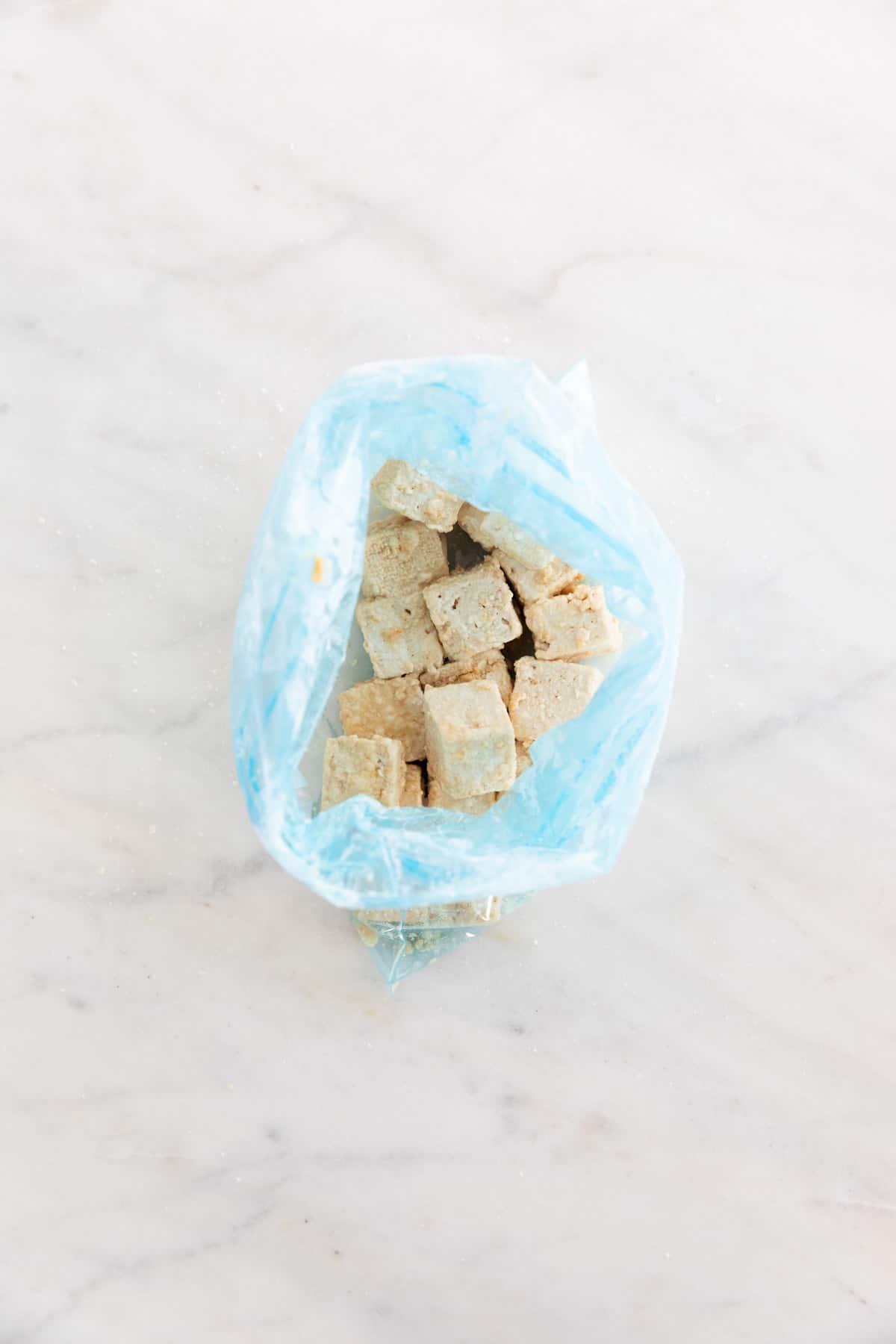 Tofu cubes coated in cornstarch inside a freezer bag.