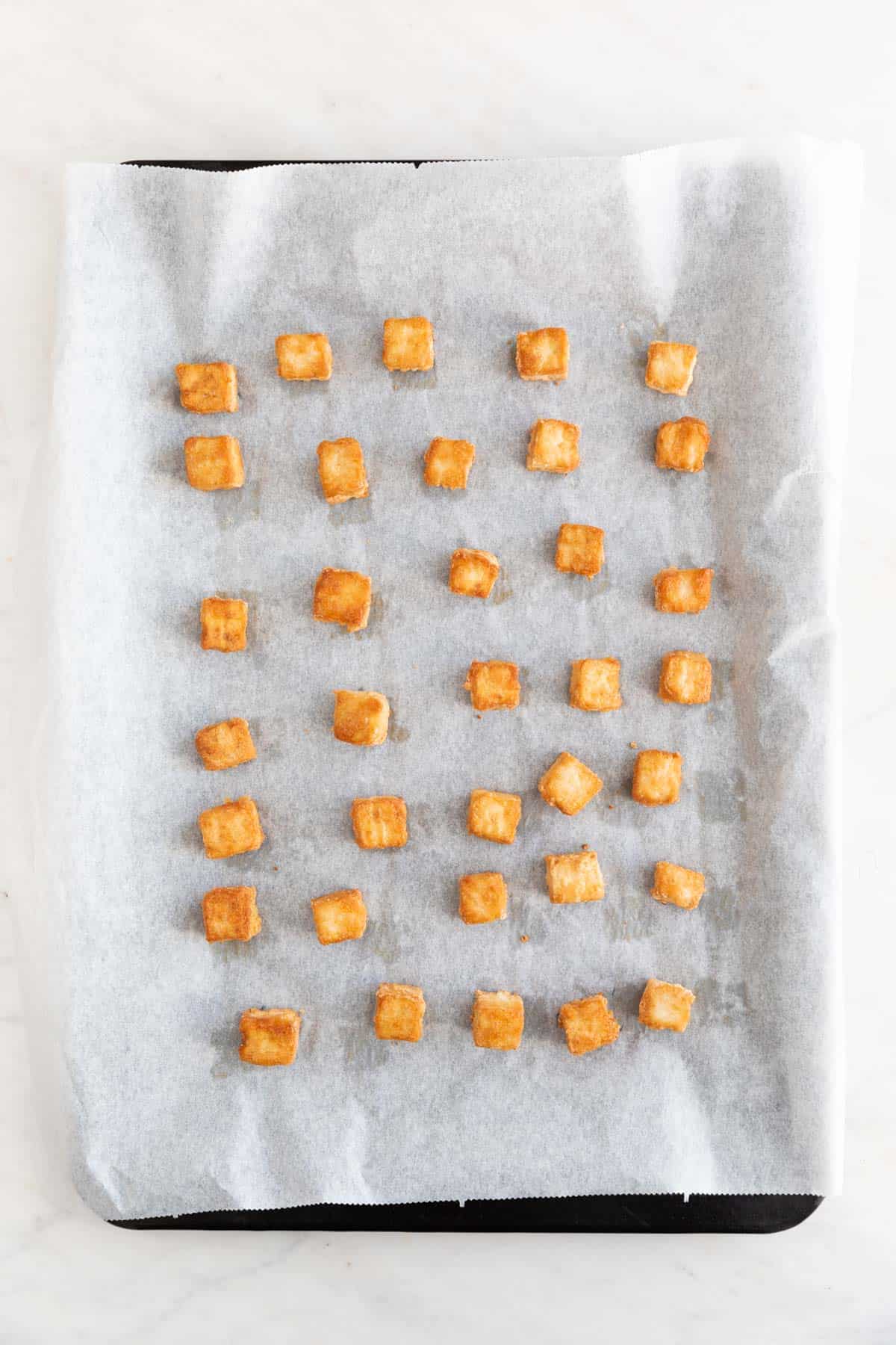 Tofu cubes onto a lined baking sheet after baking.