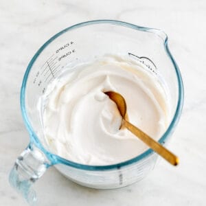 A glass measuring cup with vegan mayonnaise and a spoon.
