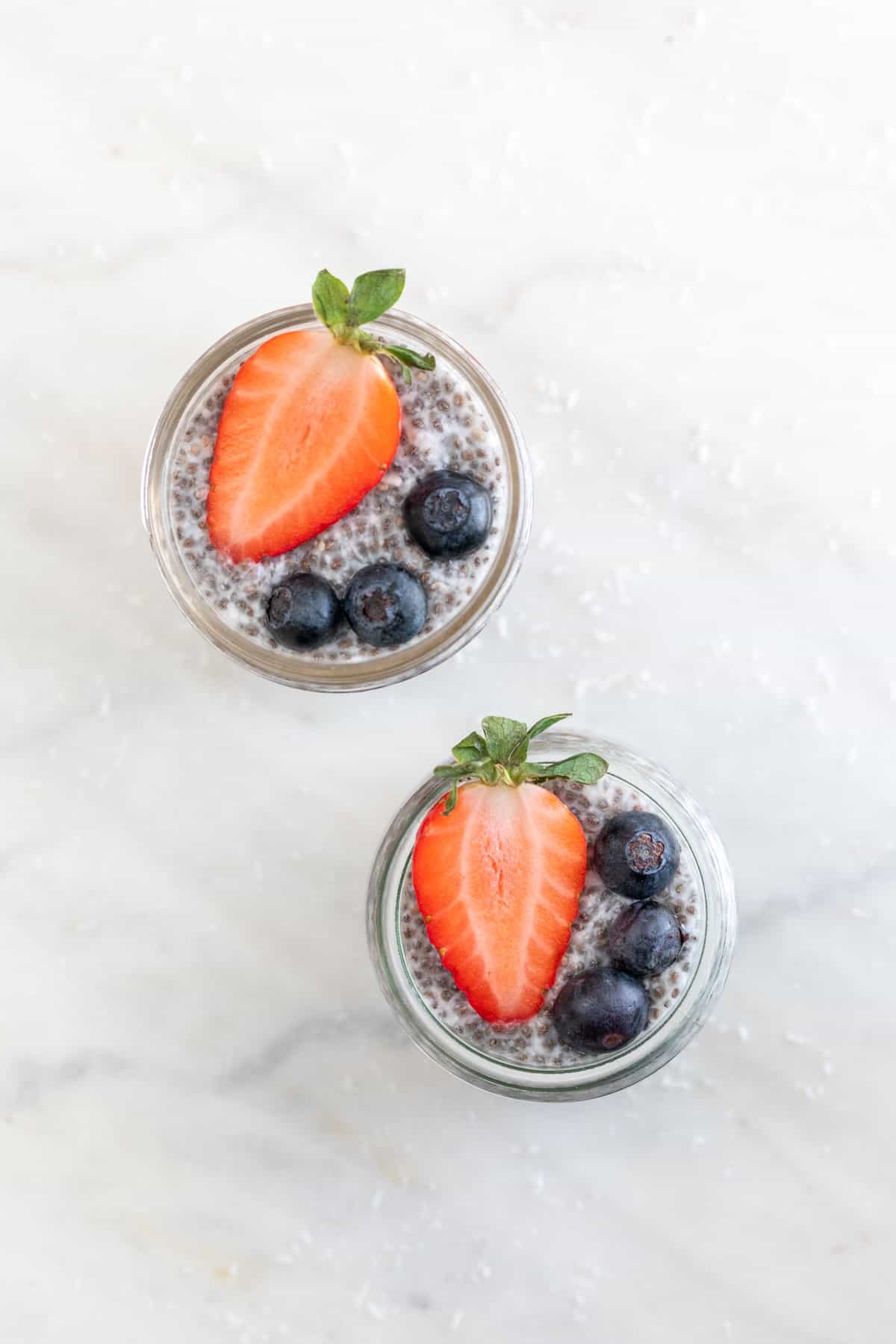 Overview of two jars with chia pudding and topped with berries.