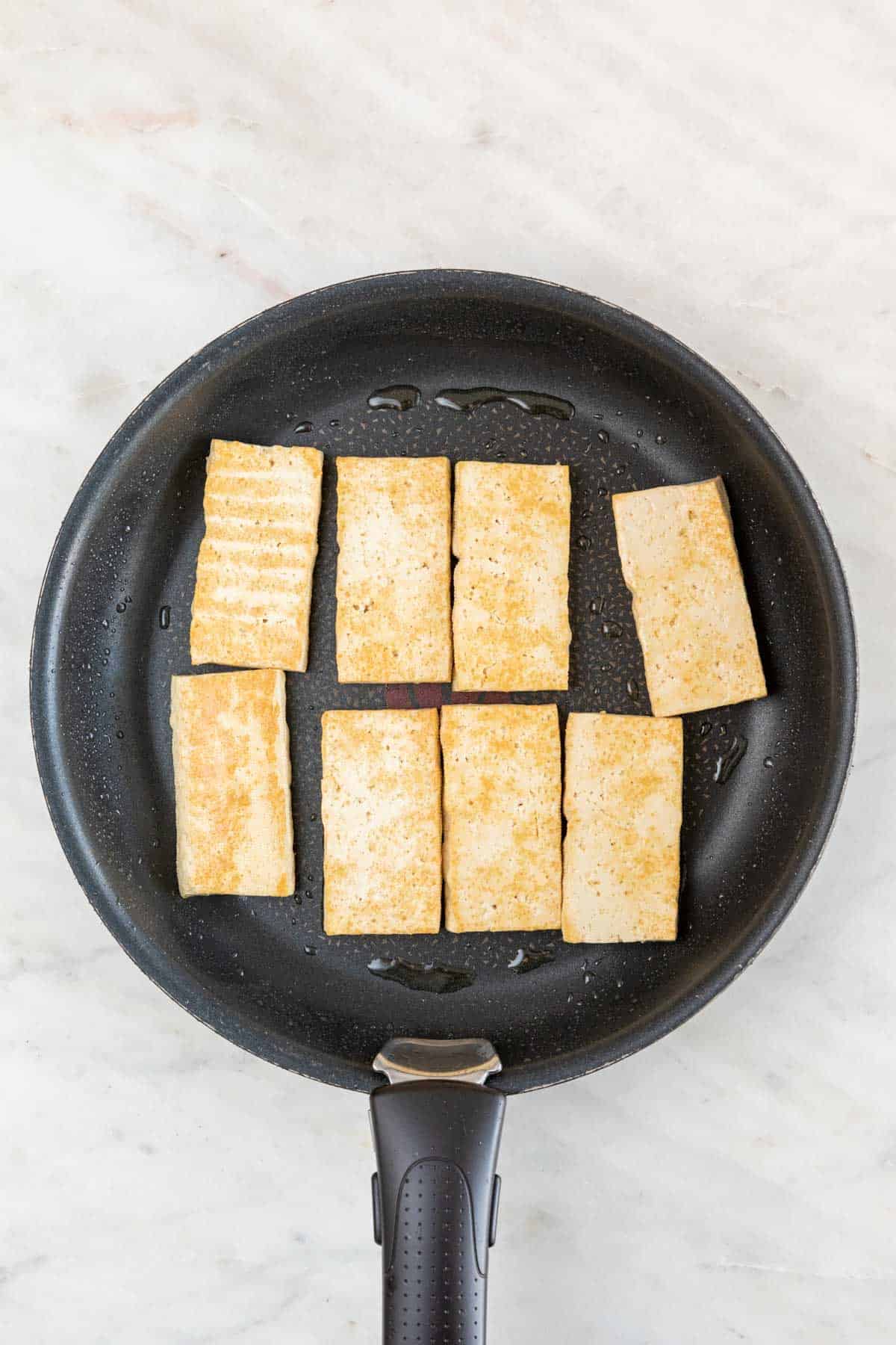 A frying pan with cooked tofu slices.