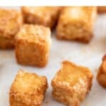 Several baked tofu cubes onto a lined baking sheet.