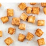 Overview of baked tofu cubes onto a lined baking sheet.