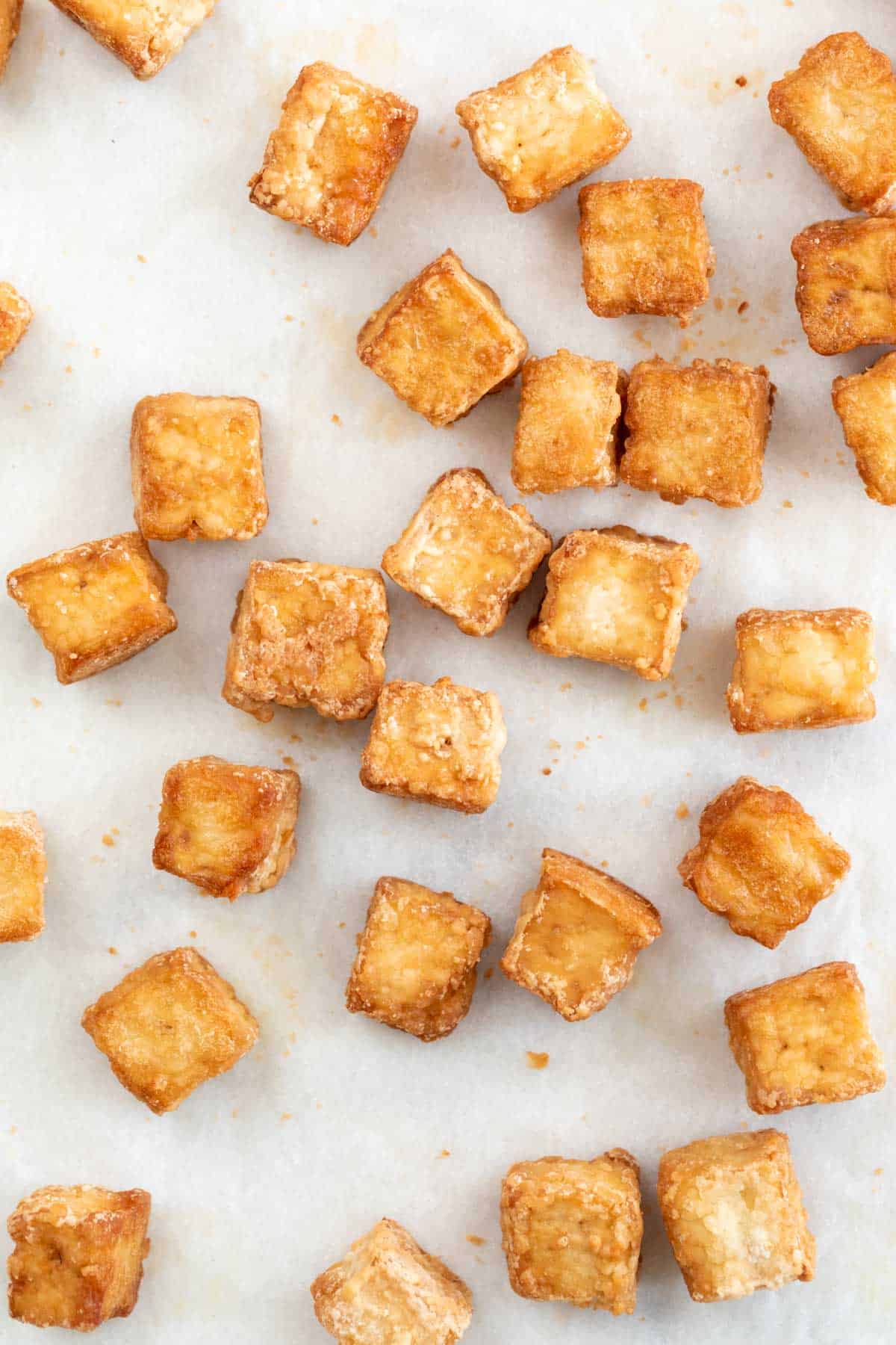 Overview of baked tofu cubes onto a lined baking sheet.