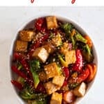 A bowl with tofu stir fry garnished with some sesame seeds.