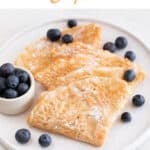 A plate with several folded vegan crepes with some blueberries and powdered sugar on top.