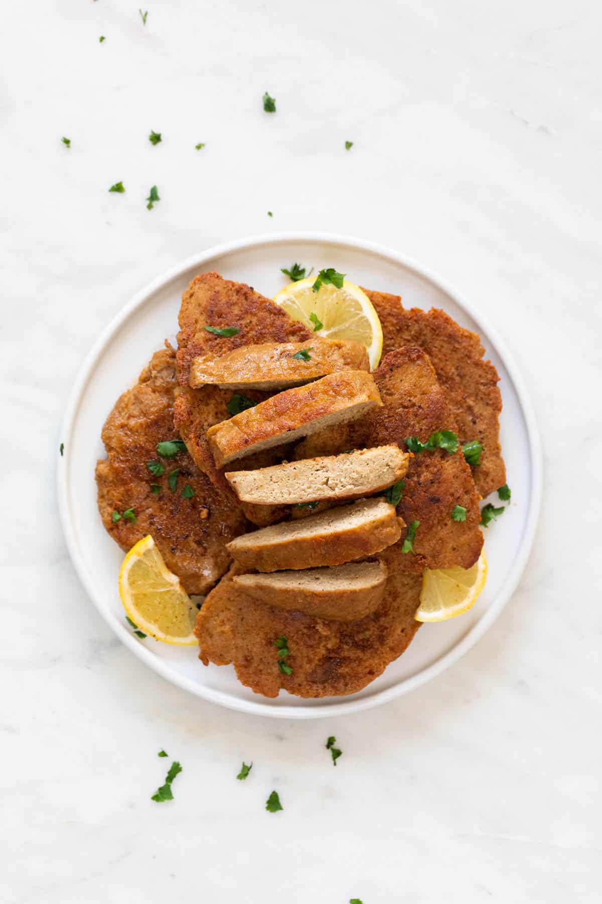 A dish with some vegan chicken fillets, one of them sliced, with some chopped cilantro and lemon slices on top.