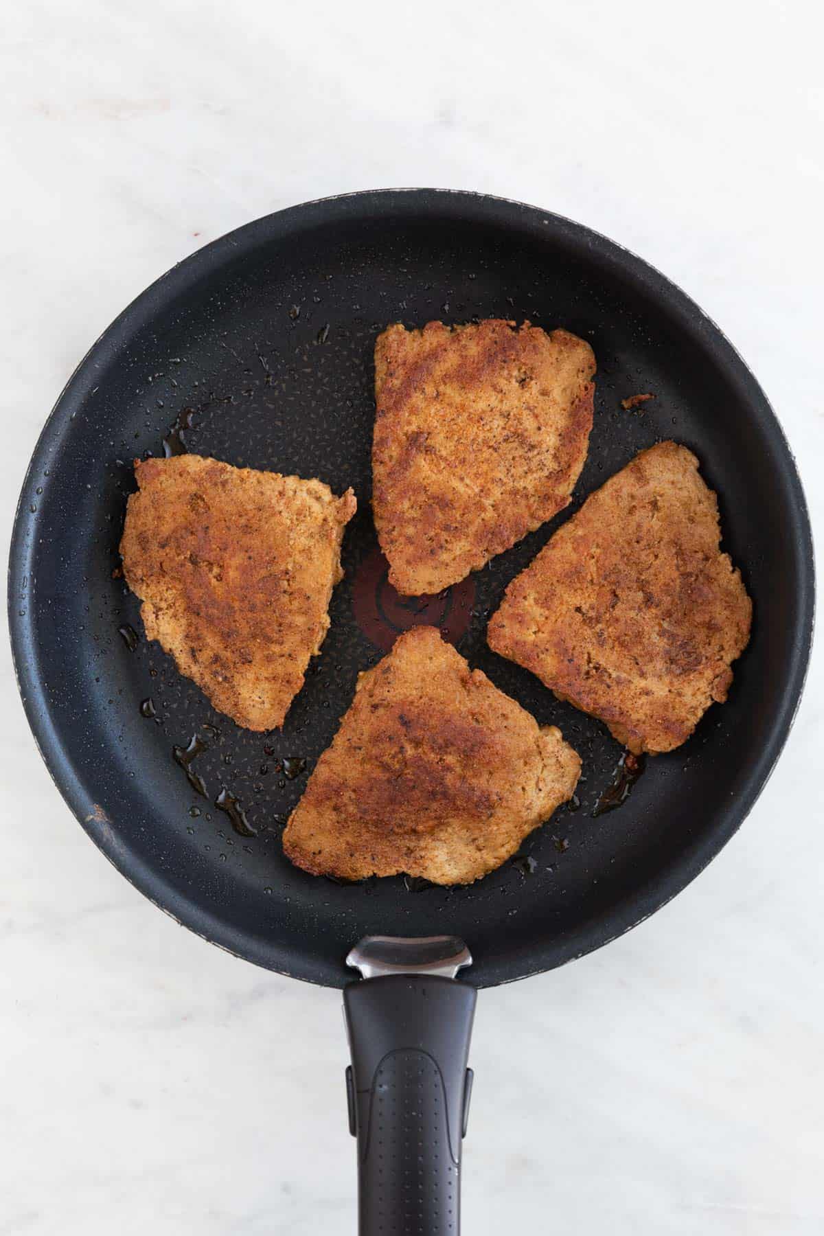 A skillet with 4 fully cooked vegan chicken fillets.