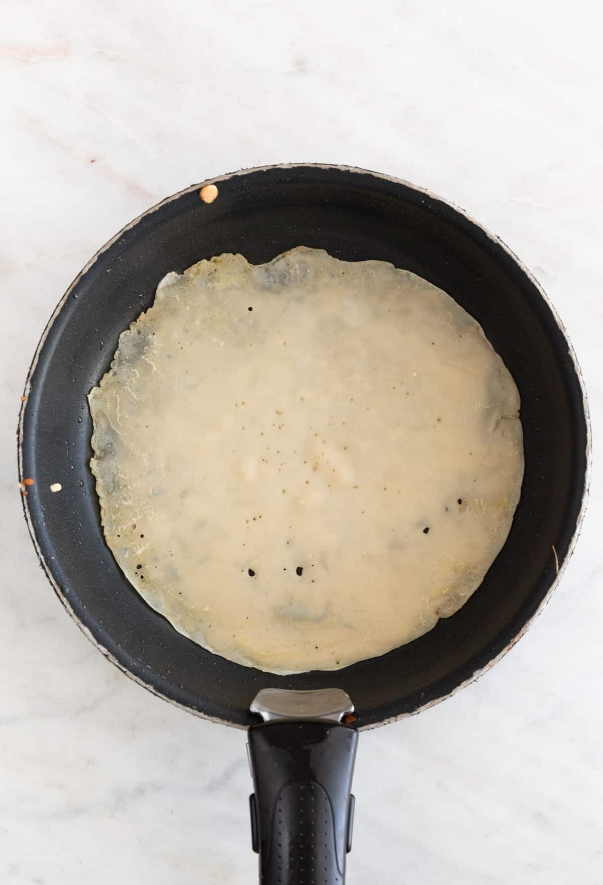 A skillet with a crepe cooked for one side.