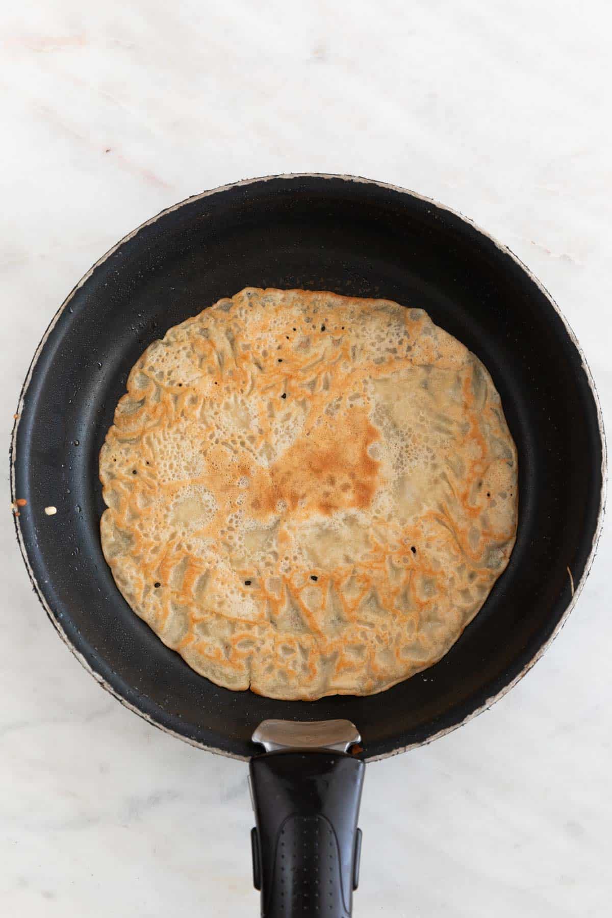 A skillet with a crepe cooked for both sides.