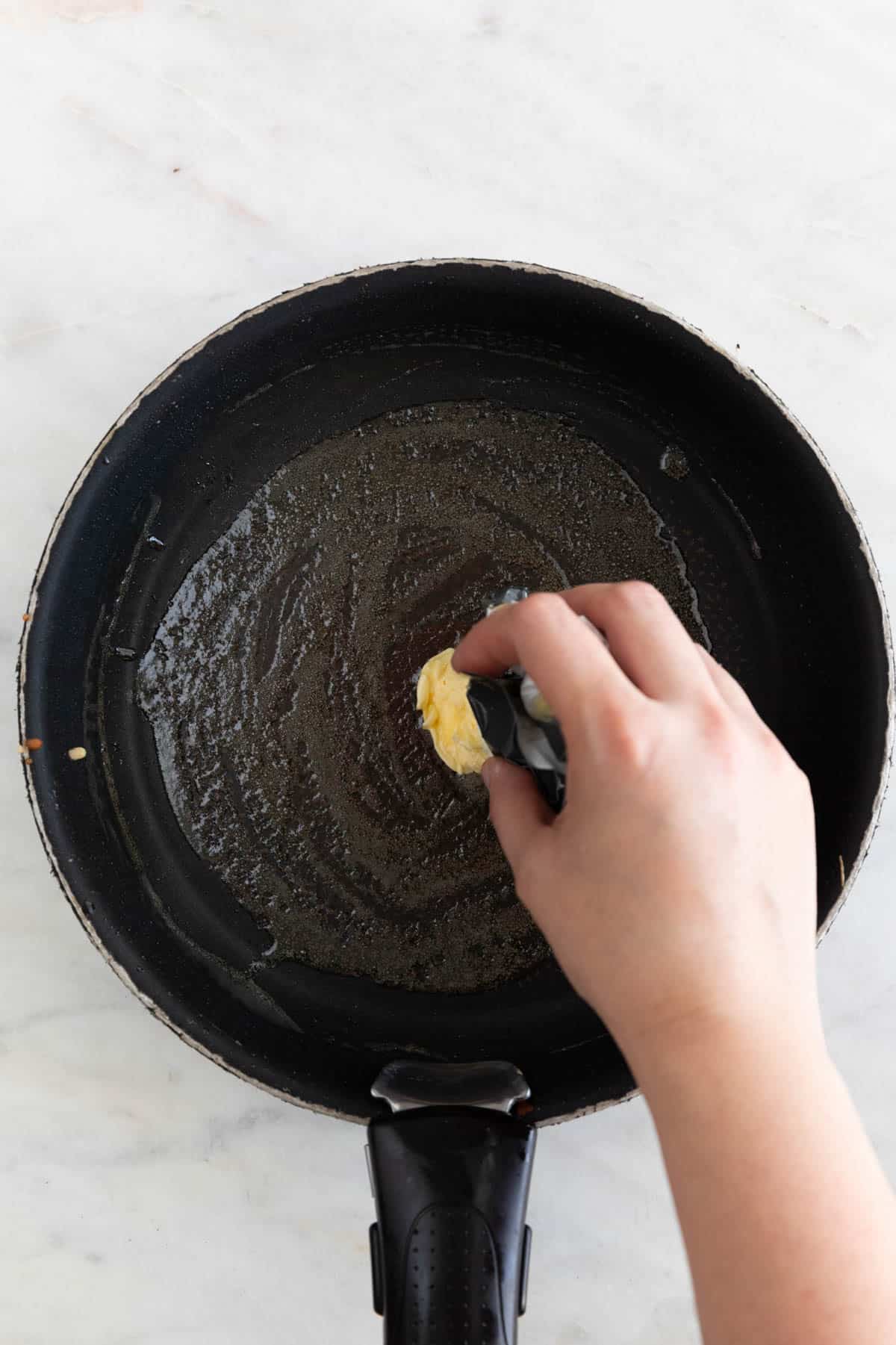 A hand rubbing a vegan butter stick on a pan.