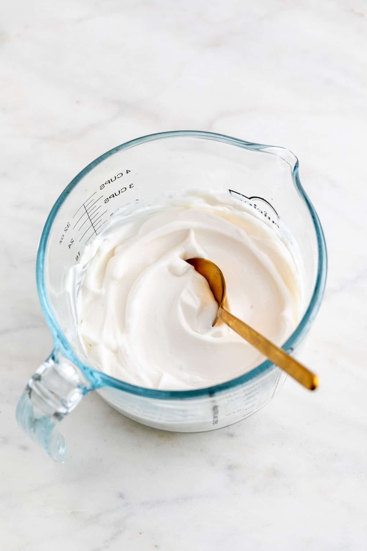 A glass measuring cup with vegan mayonnaise and a spoon.