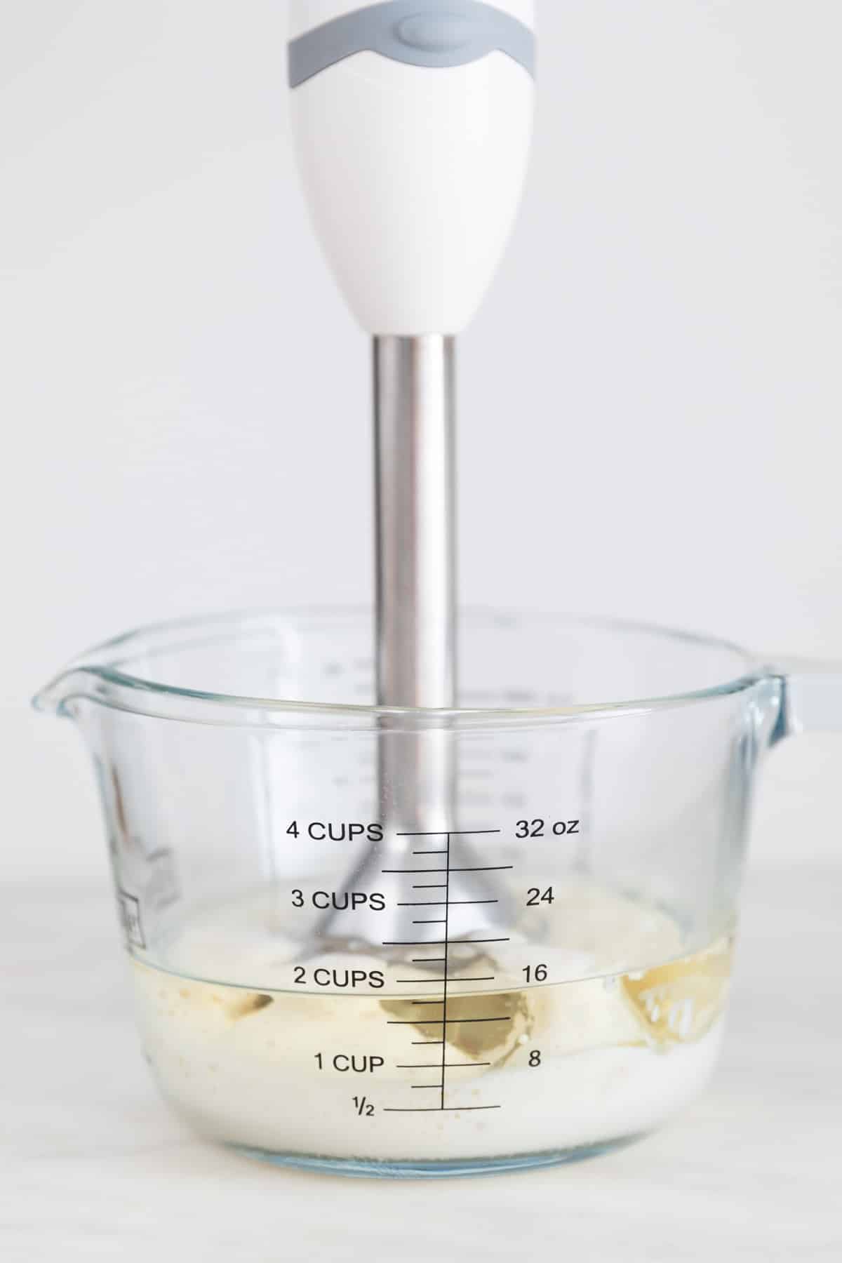 A glass measuring cup with an immersion blender sitting in the bottom before blending the vegan mayonnaise ingredients.