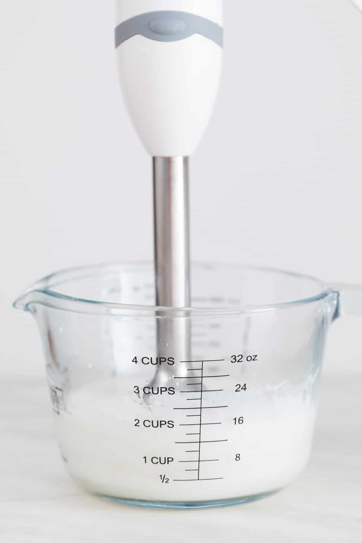A glass measuring cup with an immersion blender sitting in the bottom once the vegan mayonnaise has emulsified.