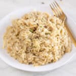 Square photo of a dish of vegan risotto topped with herbs and vegan cheese.