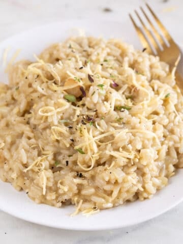 Square photo of a dish of vegan risotto topped with herbs and vegan cheese.