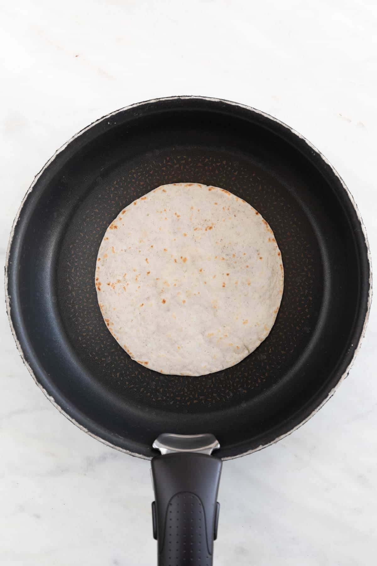 A skillet with a flour tortilla while toasting.
