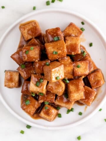 Square picture of a dish with marinated tofu garnished with chopped chives.