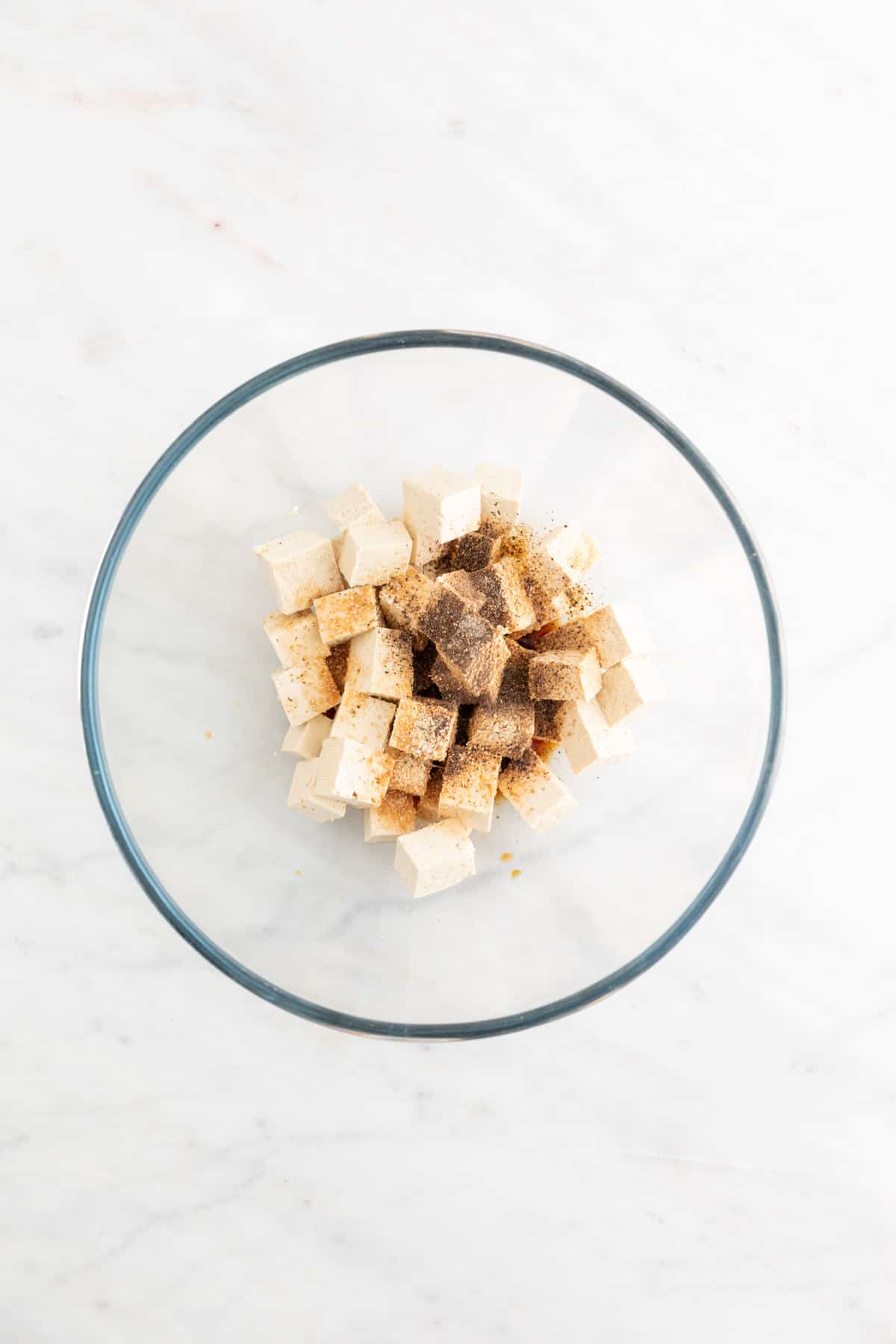 Tofu cubes in a large mixing bowl with some seasonings on top.